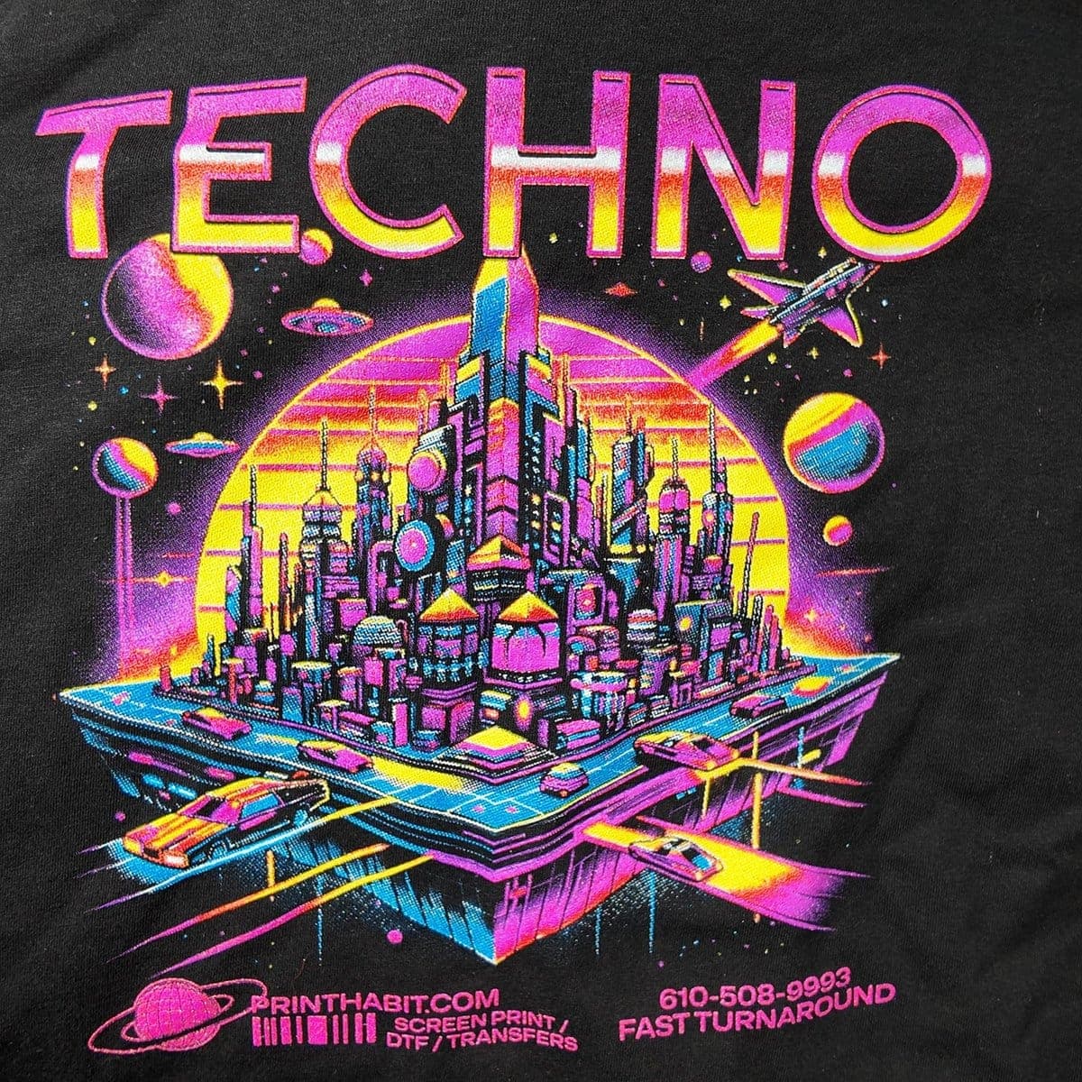 Close-up of a full-color 'TECHNO' neon city design printed on a black t-shirt by Print Habit, Coatesville PA