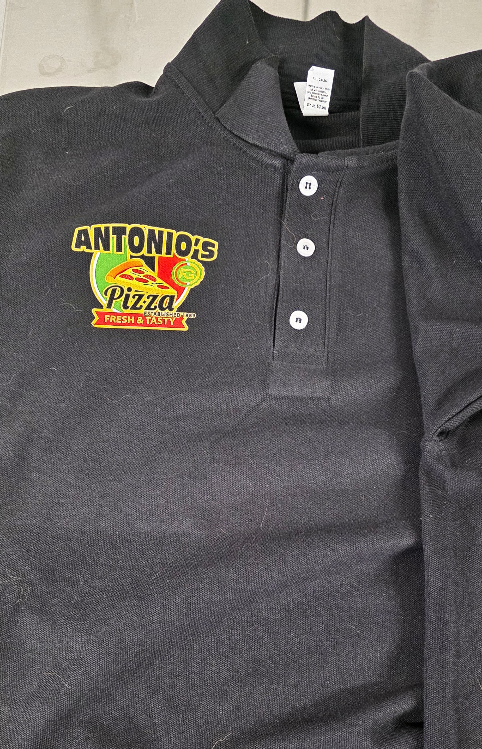 Left-chest Antonio's Pizza logo printed on a black staff polo by Print Habit