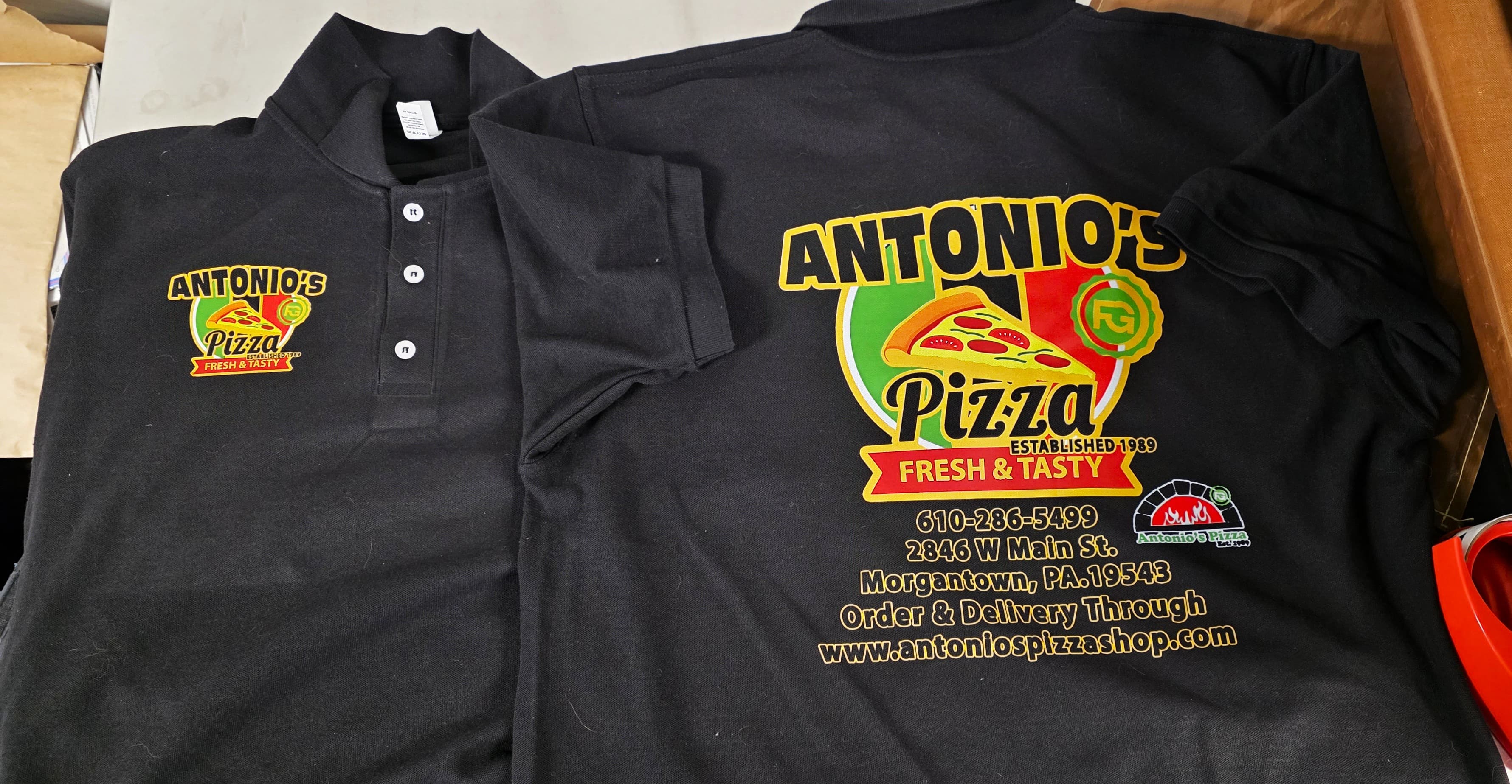 Two black Antonio's Pizza polos showing the left-chest logo and the full-color back print by Print Habit, Morgantown PA