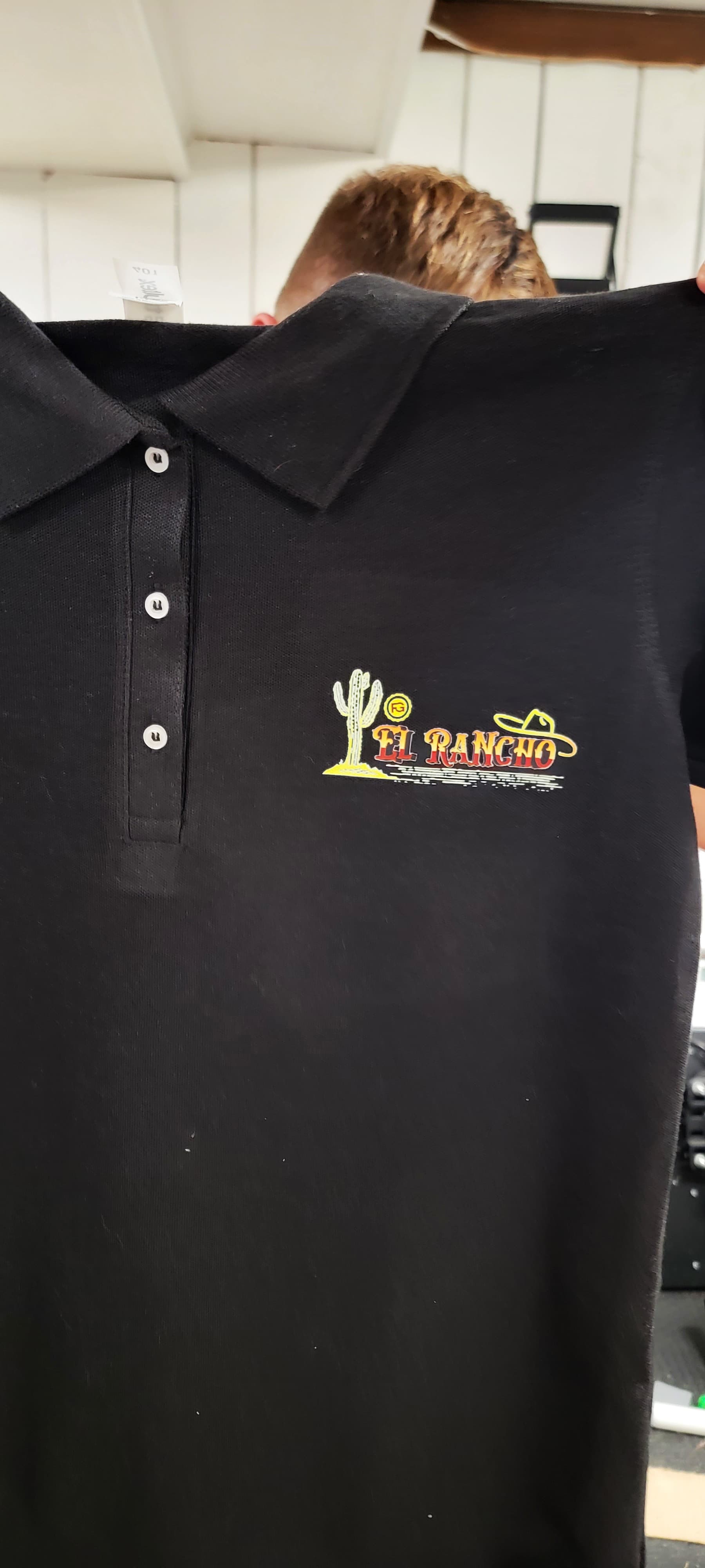 Custom black El Rancho staff polo with a full-color printed chest logo by Print Habit