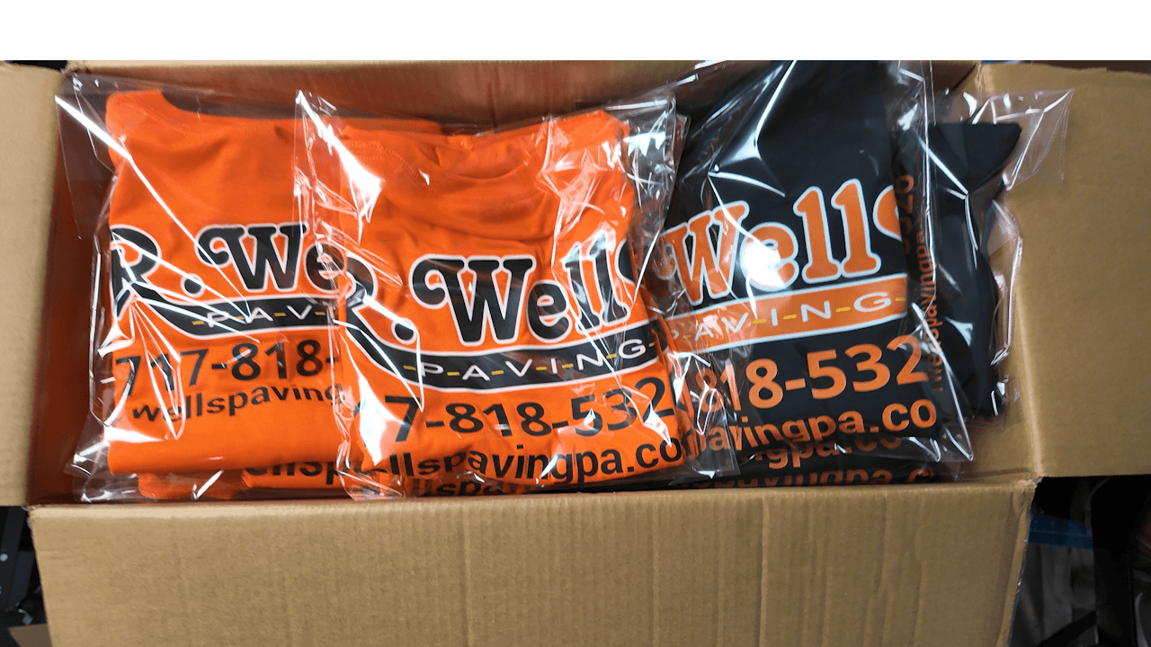 Custom DTF-printed Wells Paving business t-shirts in orange and black, folded in a fulfillment box — Print Habit, Coatesville PA