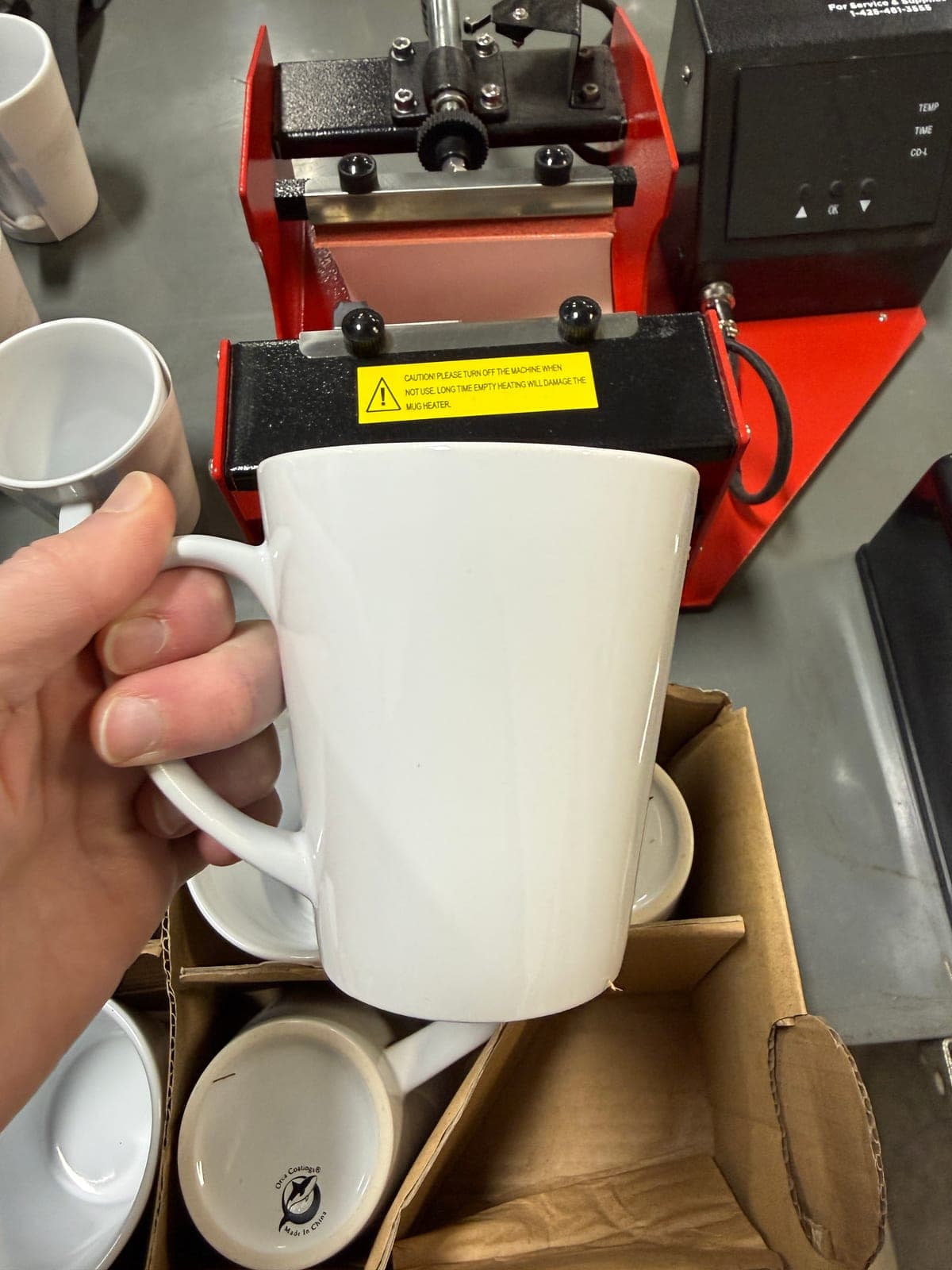 Blank white latte mug held in front of the mug press before the transfer goes on