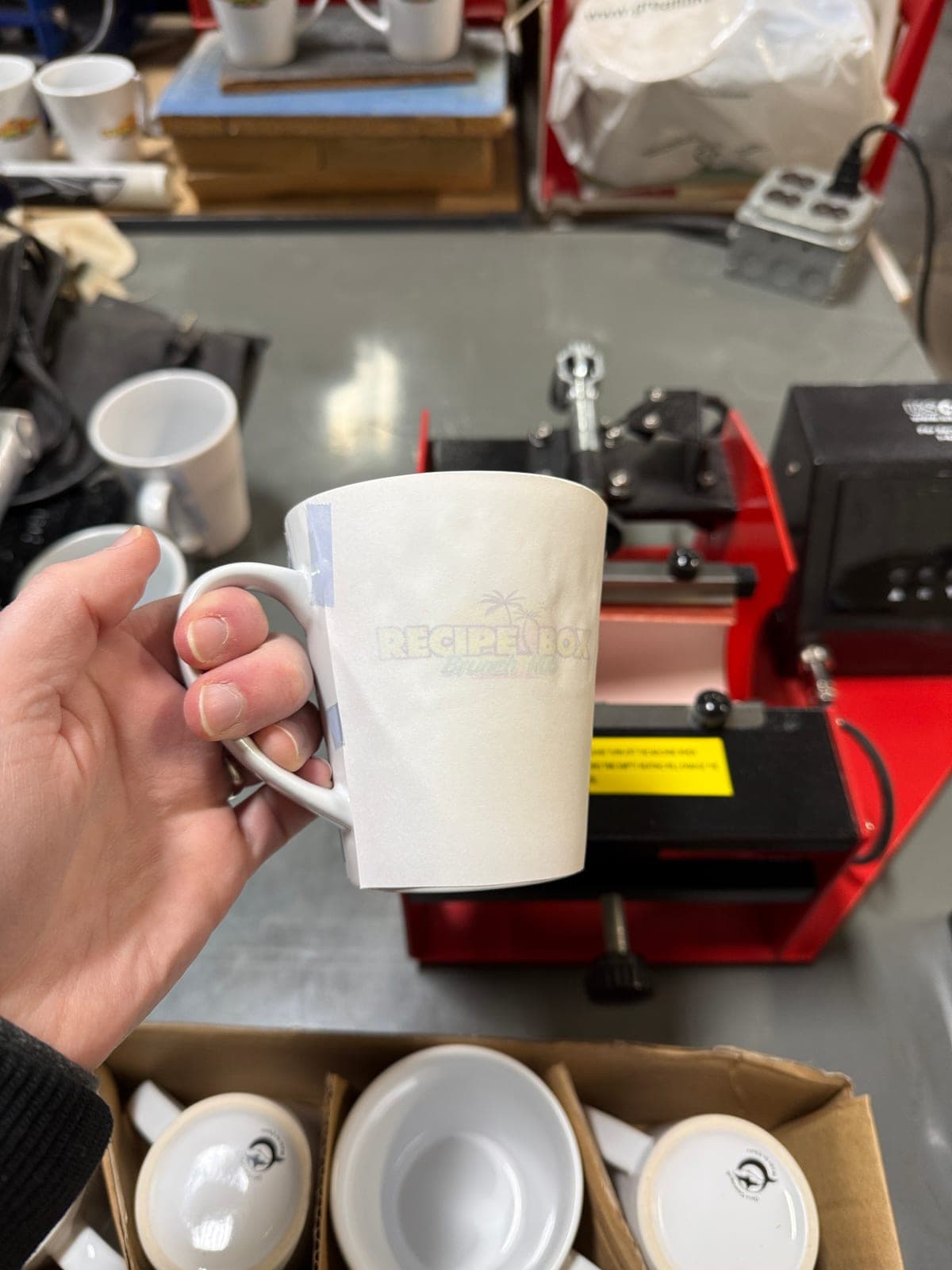 Freshly pressed mug with the sublimation transfer paper still wrapped around it, the Recipe Box design showing through