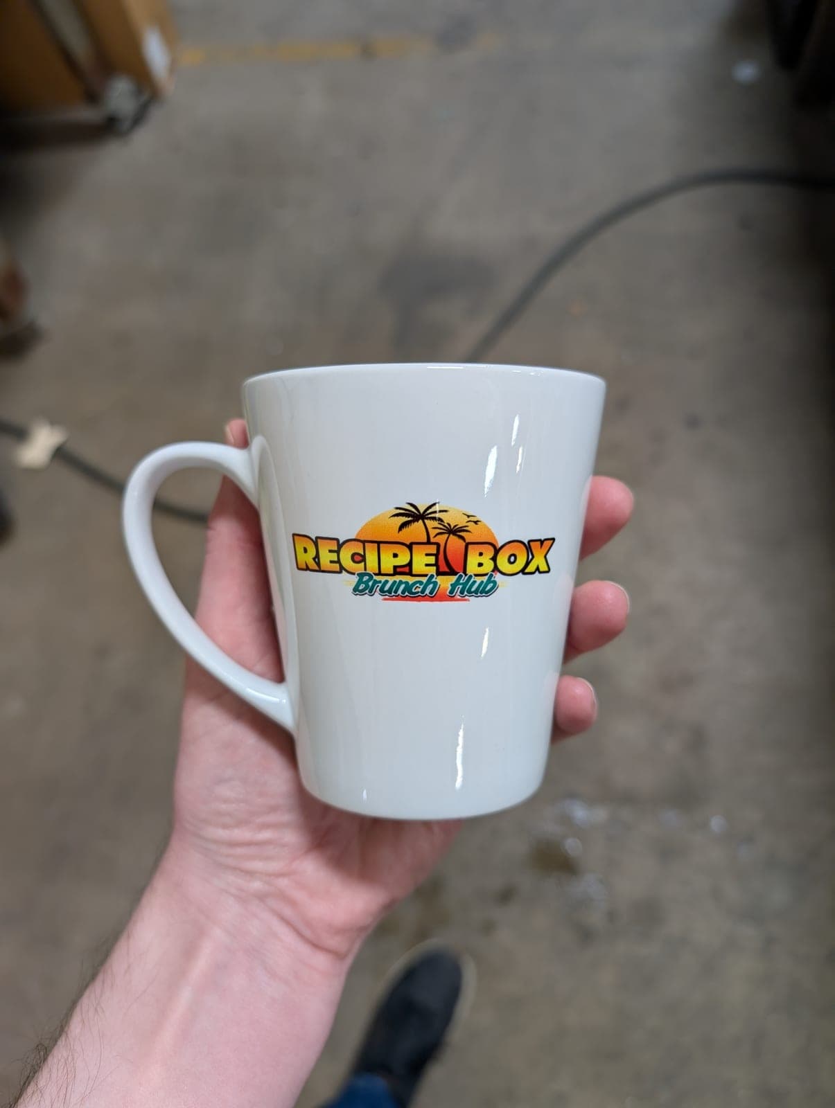 Finished Recipe Box Brunch Hub latte mug held up to show the full-color sublimated logo