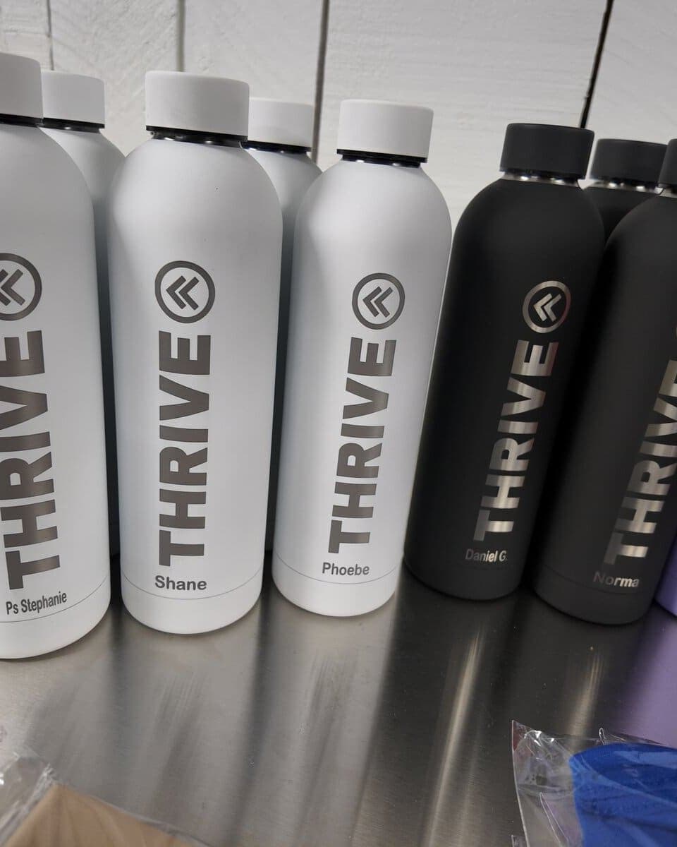 Laser-engraved water bottles with a THRIVE logo and each person's name, by Print Habit in Coatesville, PA