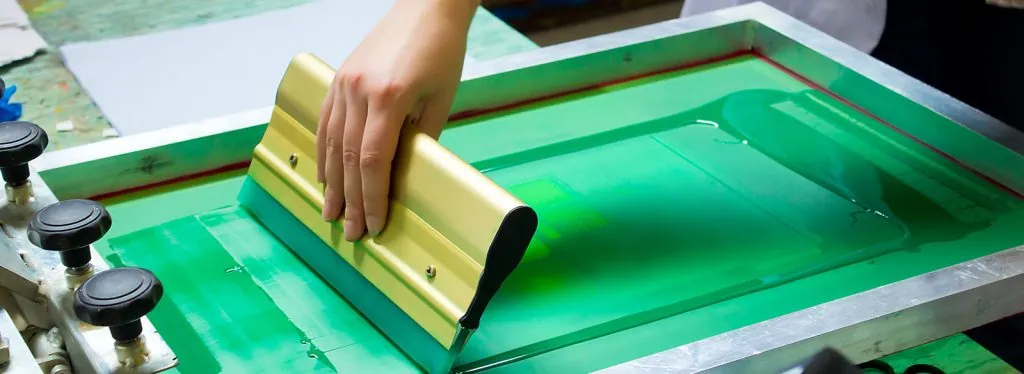 custom screen printing coatesville image show a hand pulling a screen printing squeegee across a screen in coatesville pa