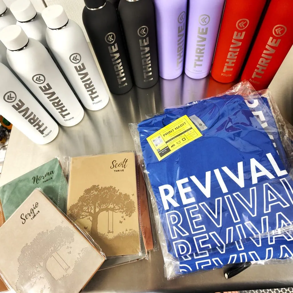 picture of custom merch and promotional items like t-shirts, tumblers, and custom leatherette notebooks personalized with names
