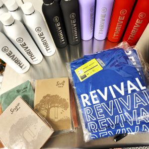 picture of custom merch and promotional items like t-shirts, tumblers, and custom leatherette notebooks personalized with names