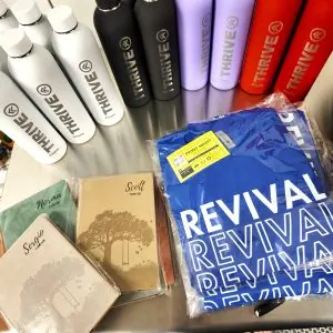 picture of custom merch and promotional items like t-shirts, tumblers, and custom leatherette notebooks personalized with names